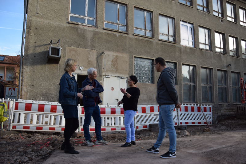 Zwei Frauen und zwei Männer im Gespräch miteinander; im Hintergrund ein Bauzaun vor einem erkennbar altem Gebäude