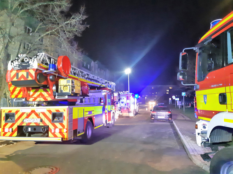 Mehrere Feuerwehren stehen am Abend vor einem Wohngebäude.