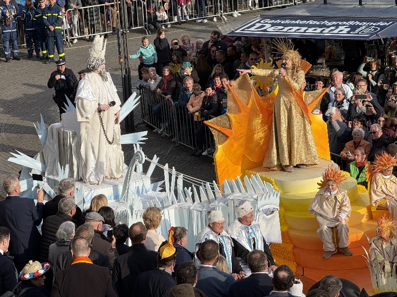 Eine als Sonne verkleidete Frau zeigt auf einen als Winter verkleideten Mann. Darum herum stehen viele Menschen.