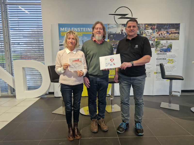 Eine Frau und zwei Männer stehen vor einer Werbe-Wand für Opel. Sie halten Zettel in den Händen.