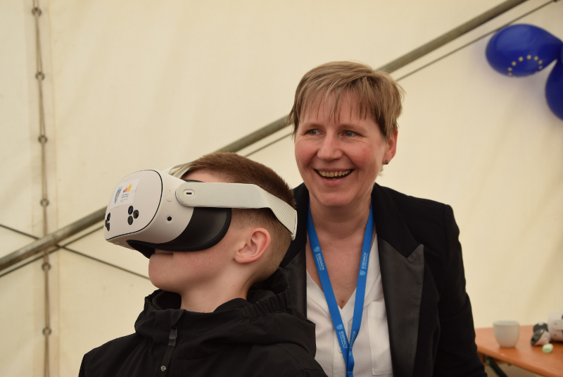 Ein Junge trägt eine VR-Brille. Hinter ihm freut sich eine Frau.
