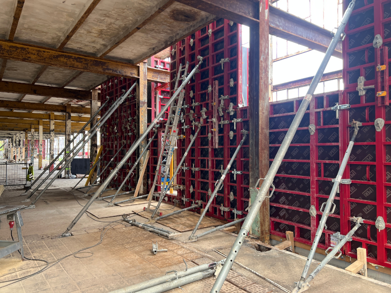 Rote Metallschalungen stehen in einer alten Fabrikhalle. Sie werden mit Metallstangen gestützt.