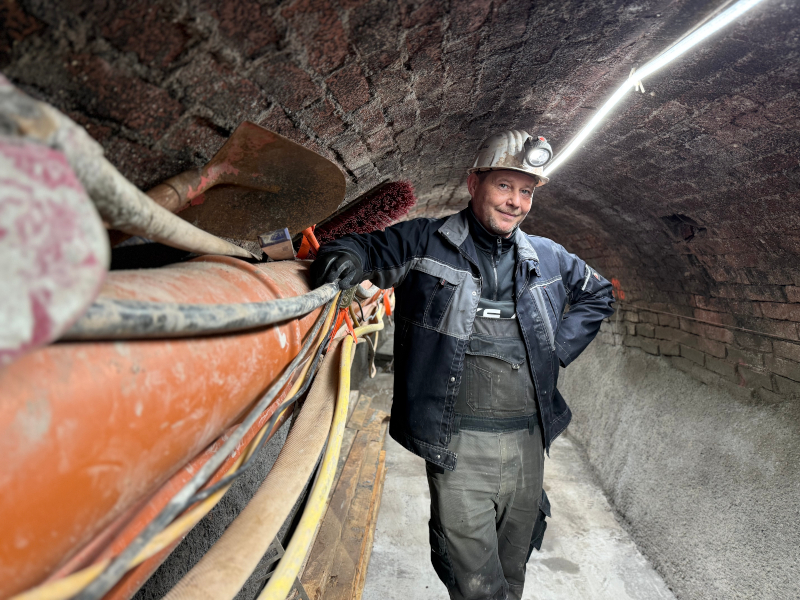 Ein Bauarbeiter mit Helm steht in einem Gewölbe. Links von ihm sind viele Leitungen an der Wand entlang verlegt.