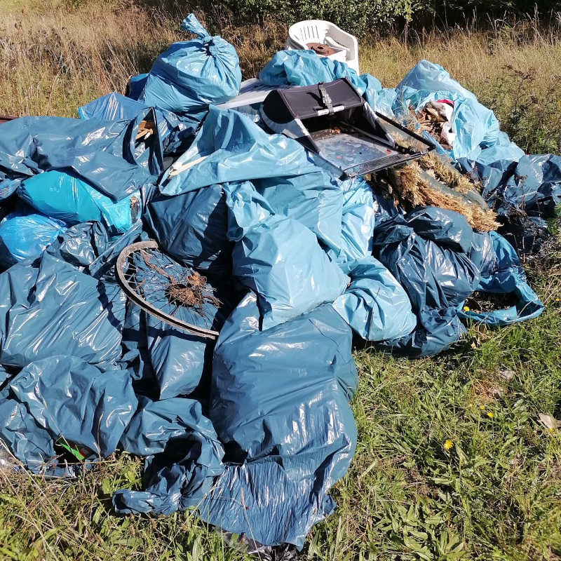 Viele blaue Müllsäcke, die gefüllt sind, liegen auf einem Haufen. Auch ein Gartenstuhl aus Plastik und Teile eines Grills sind dabei.
