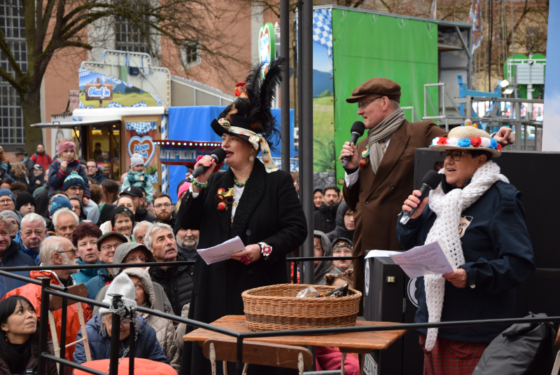 Zwei Frauen und ein Mann stehen auf einem Wagen mit Mikros in der Hand. Dahinter viele Menschen.
