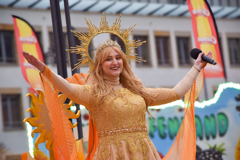 Eine als Sonne verkleidete Frau breitet ihre Arme aus und lächelt.