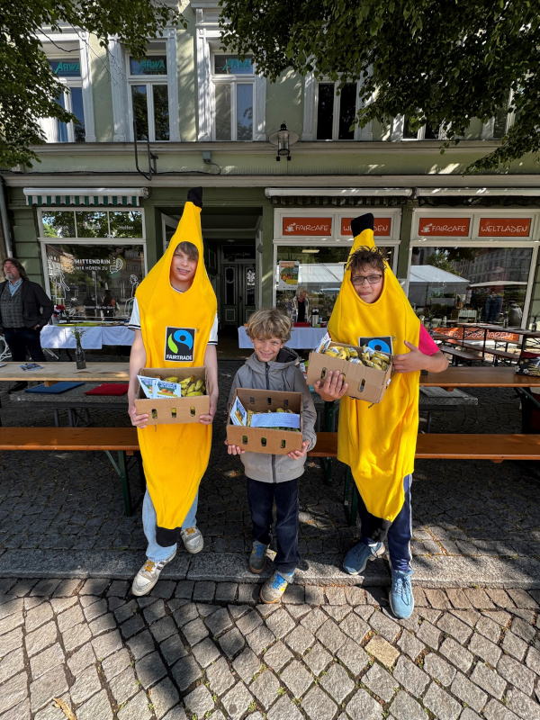 Drei Jungen stehen in Bananen-Kostümen vor einem Geschäft.