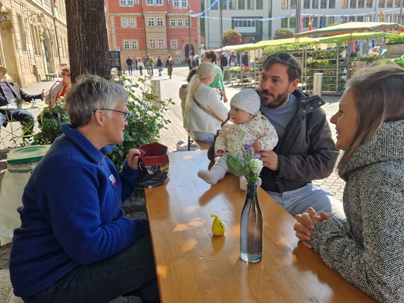 Eine Familie sitzt an einem Biertisch und unterhält sich mit einer älteren Frau.