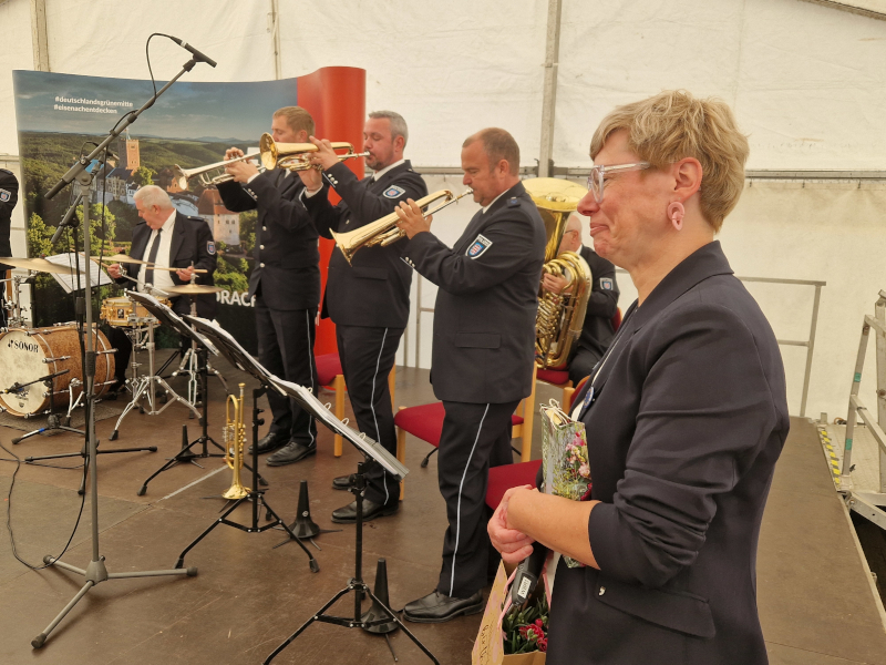 Eine Frau steht auf einer Bühne; dahinter Musiker.