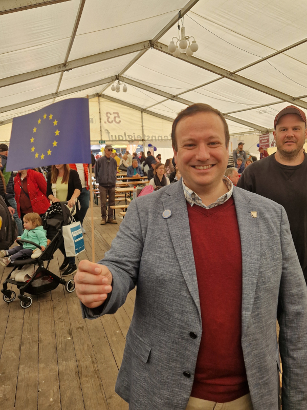 Ein Mann in einem Jacket hält ein Europa-Fähnchen.