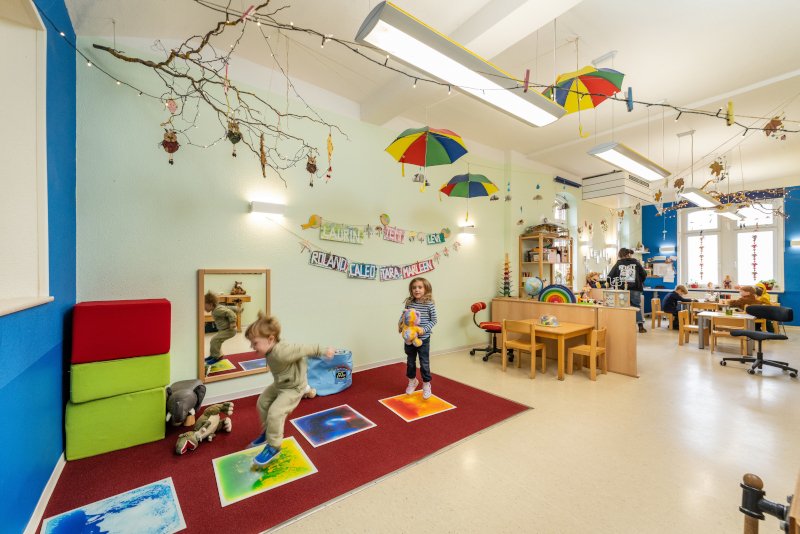 Spielzimmer eines Kindergartens mit Kindern, Holzmöbeln und Spieleteppich