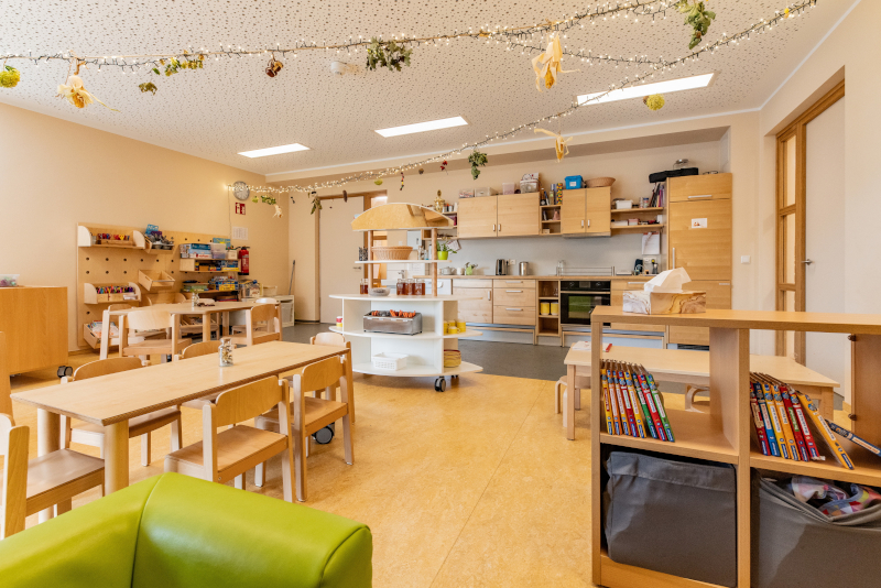 Ein Gruppenraum mit Tischen, Stühlen und gefüllten Regalen mit Büchern und Bastelmaterialien