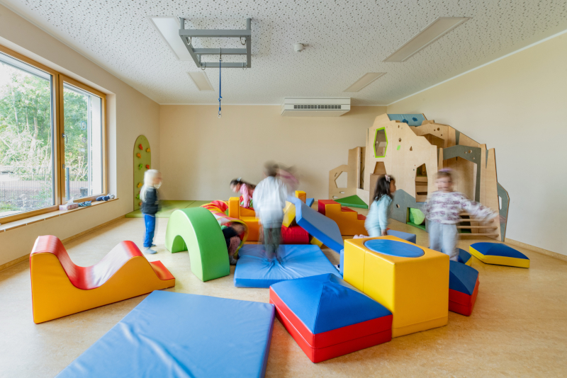 Ein Gruppenraum mit Spiel- und Klettermöbeln an denen mehrere Kinder spielen