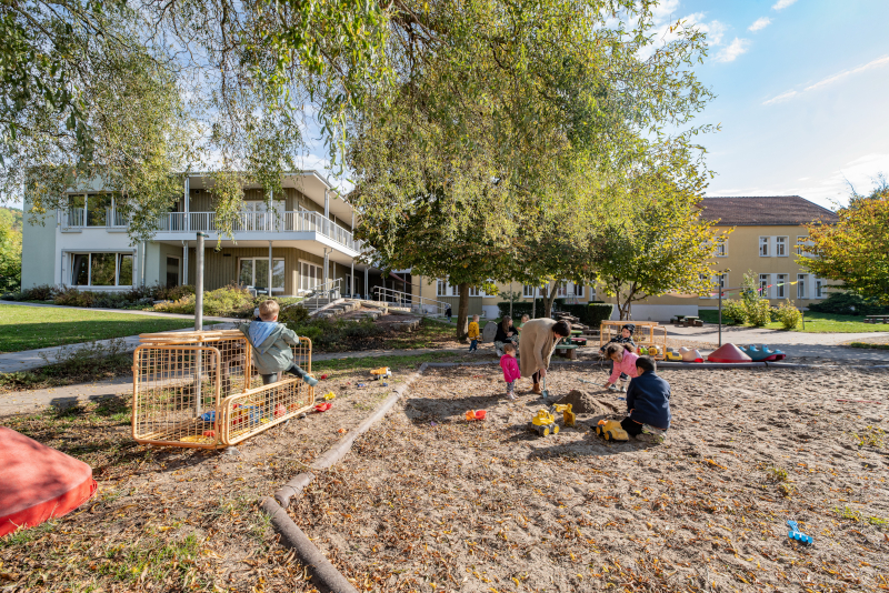 Kinder spielen im Sandkasten mit Bäumen und Gebäuden im Hintergrund