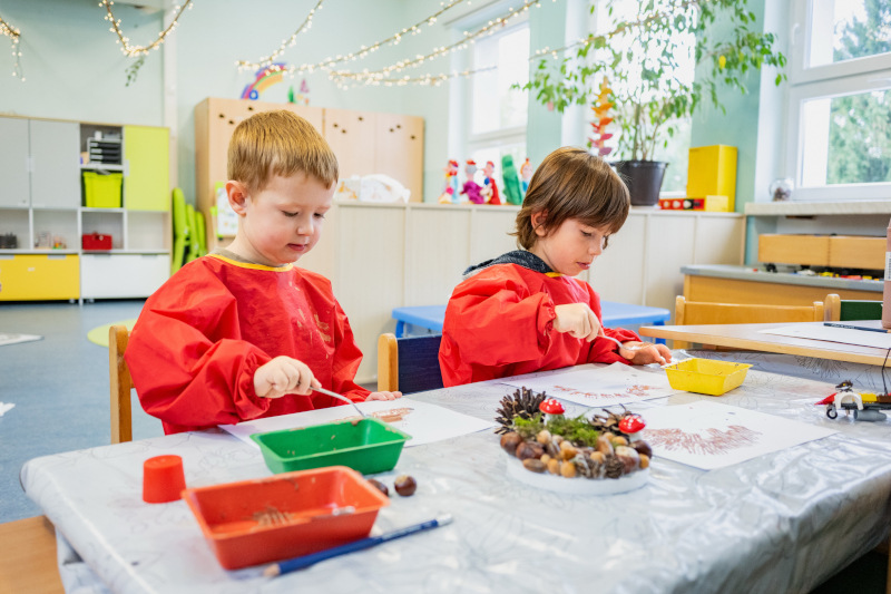 Zwei Jungen sitzen an einem Tisch und spachteln. Auf dem Tisch liegen Naturmaterialien zum Basteln.