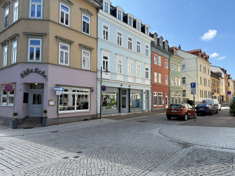 Eine Kreuzung mit Häusern. Am Rand der Straße parken Autos.