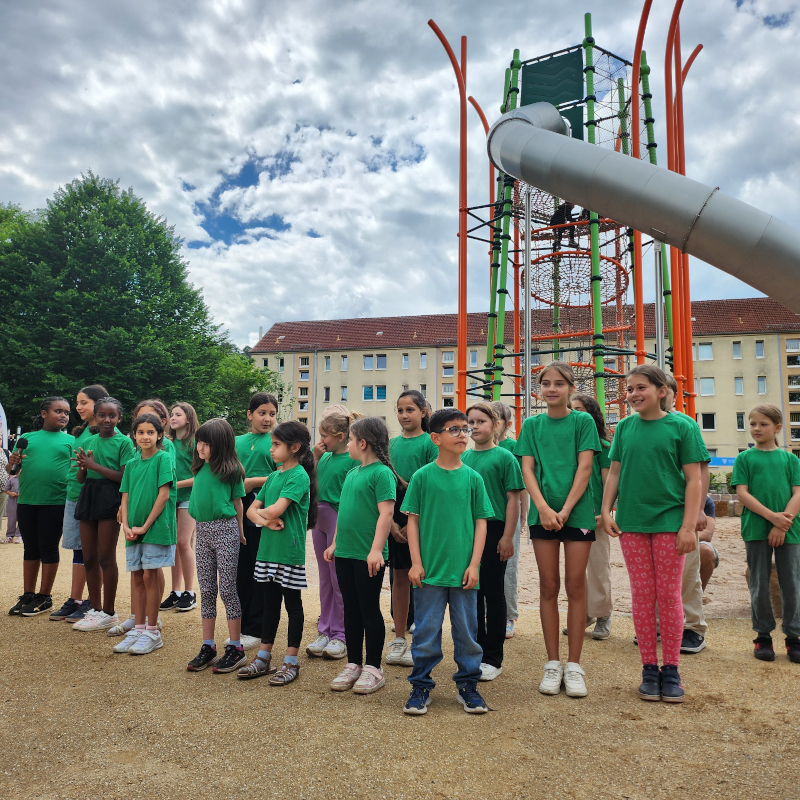 Kinder in grünen T-Shirts stehen vor einem großen Spielturm