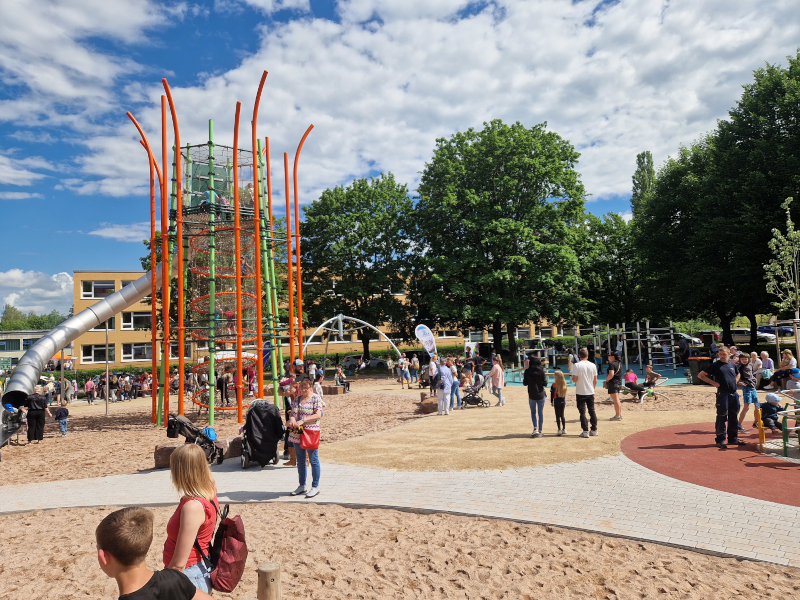 Ein großer Spielturm mit Rutsche und viele Kinder und Erwachsene drum herum.