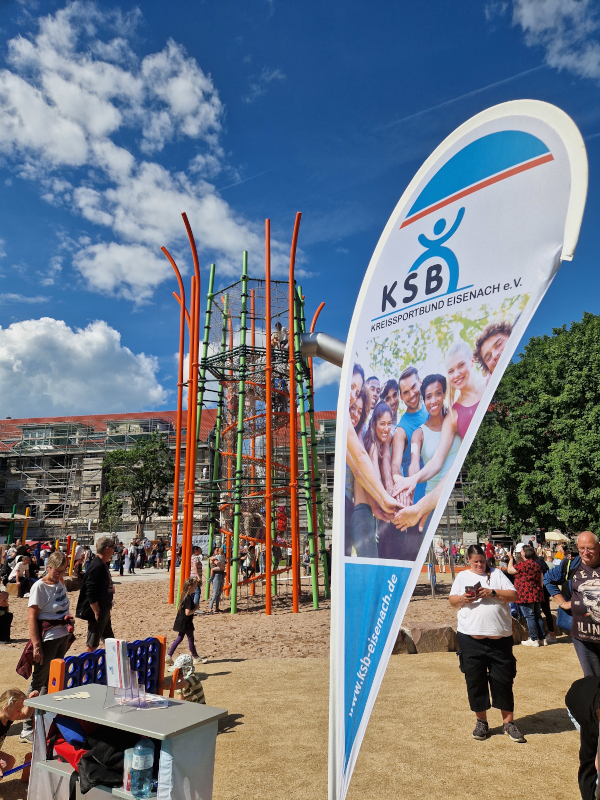Kinder spielen im großen Spielturm und im Vordergrund steht eine Flagge vom Kreissportbund Eisenach.